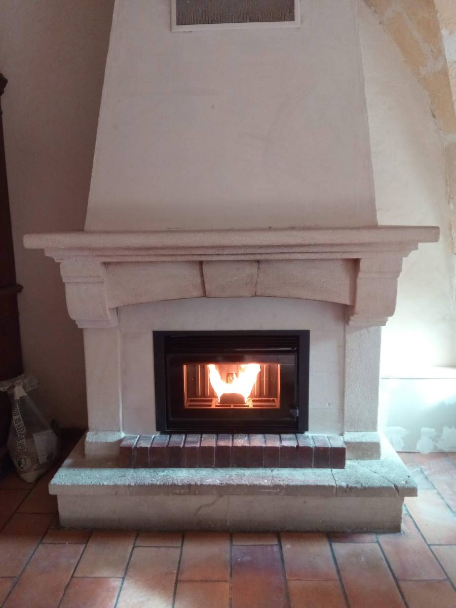 Vision du feu dans un insert à granulés installé dans une ancienne cheminée en pierre à Paradou
